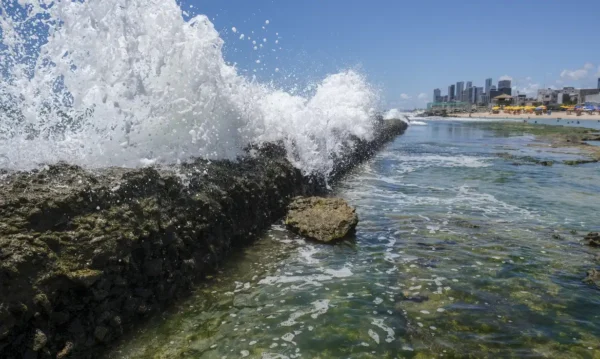 Recife(PE), 24/10/2023 - Explosão de ondas nos recifes costeiros na praia do Buraco da Véia, com a orla de Boa Viagem ao fundo, funcionando como barreira natural. As formações rochosas absorvem até 96% do impacto das ondas. Foto: Fernando Frazão/Agência Brasil