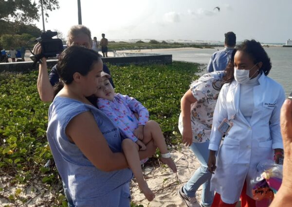Nos braços da mãe, Ana Laura foi conduzida até a beira do mar pela primeira vez — Foto: Sérgio Henrique Santos/Inter TV Cabugi