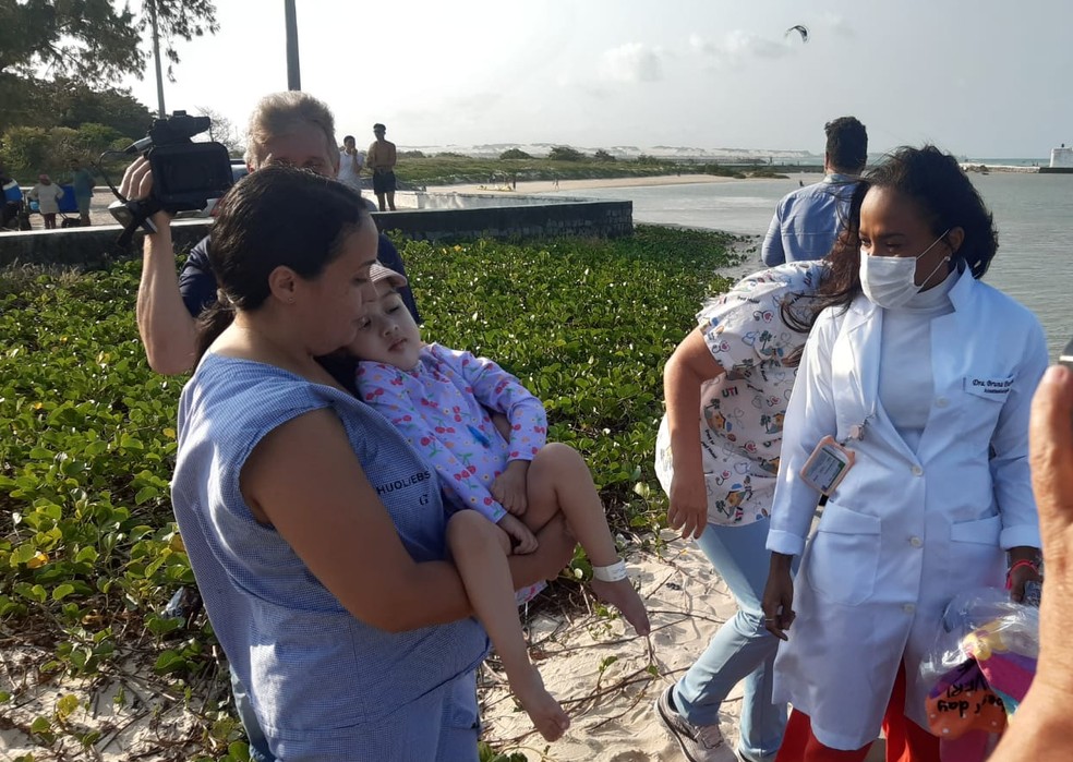 Nos braços da mãe, Ana Laura foi conduzida até a beira do mar pela primeira vez — Foto: Sérgio Henrique Santos/Inter TV Cabugi